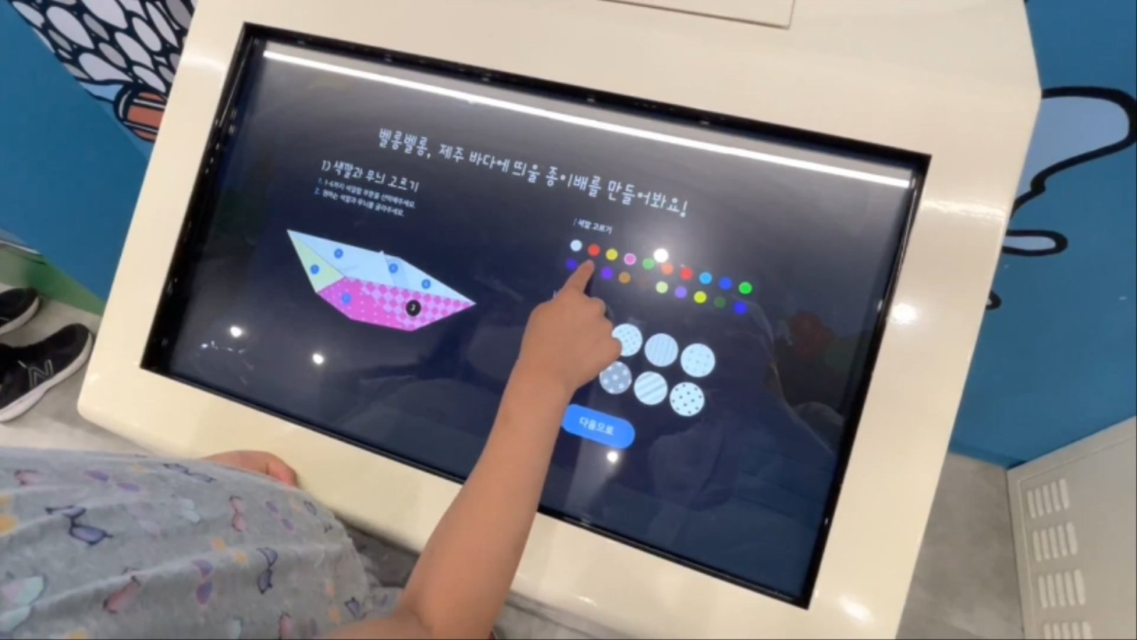 '포구의 풍경(도대불 종이배 접기)'은 7,000안시 빔프로젝터로 구현한 4,000×2,500mm 스크린과 QR코드 리더기로, 직접 접은 종이배 도안을 스캔해 화면 속 바다에 띄우는 인터랙티브 콘텐츠입니다.